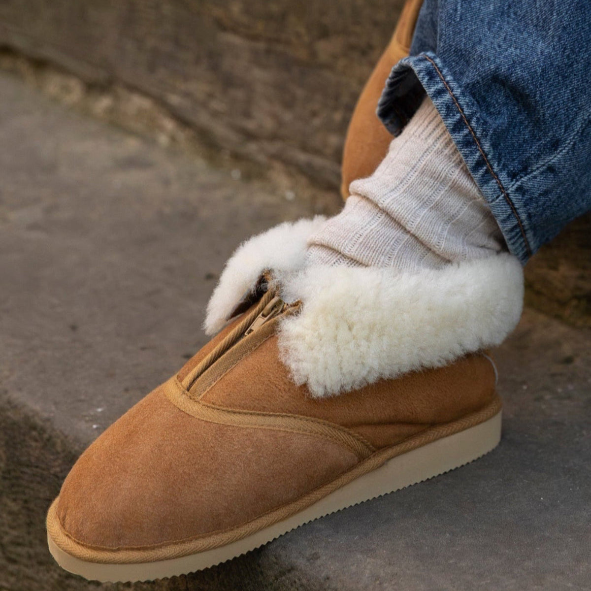 Person wearing brown shoes with white fur trim and blue jeans sitting on steps.